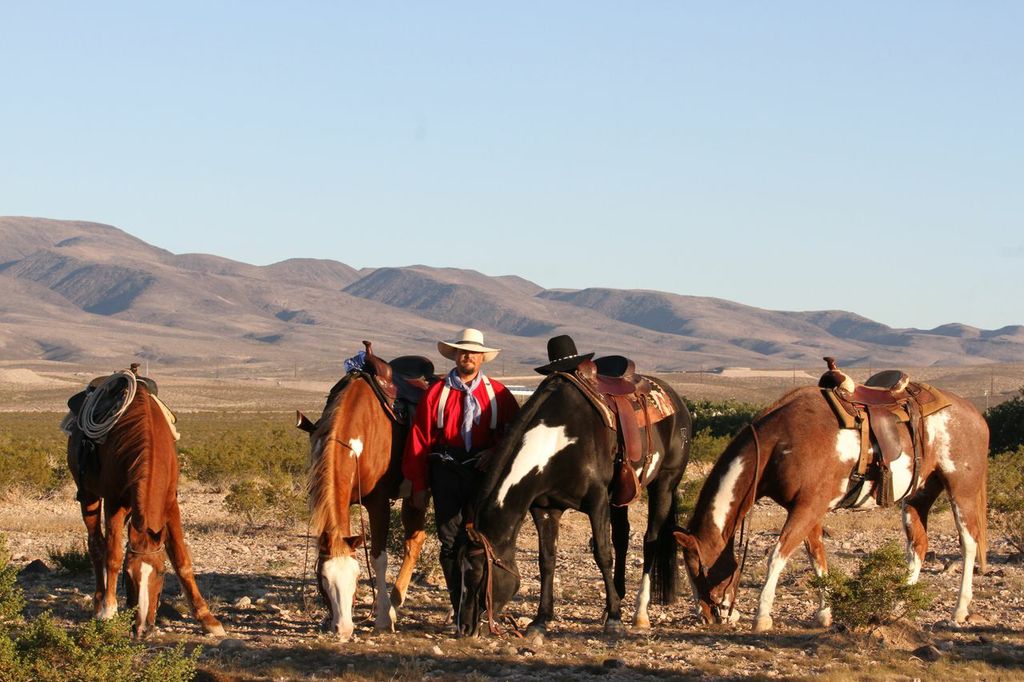Mark standing in the desert with four horses, mountain background.